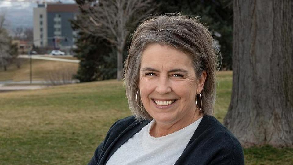 Stacey Hunter sitting on a bench in a park. She is wearing a white long sleeve t-shirt with a dark navy sweater over it and jeans. She is smiling. External link: (https://healthcare.utah.edu/patient-stories/university-of-utah-heath-neurosurgeons-remove-montana-mothers-complex-benign-brain)